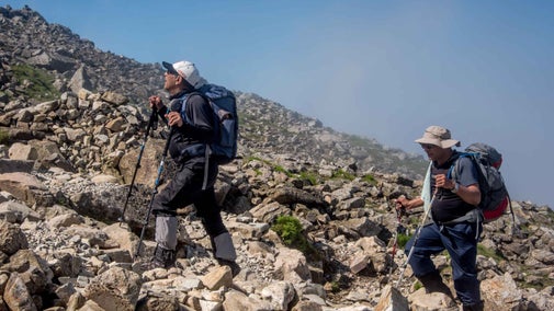 Two walkers with hiking poles crossing over stones while ascending Scafell Pike, Lake District